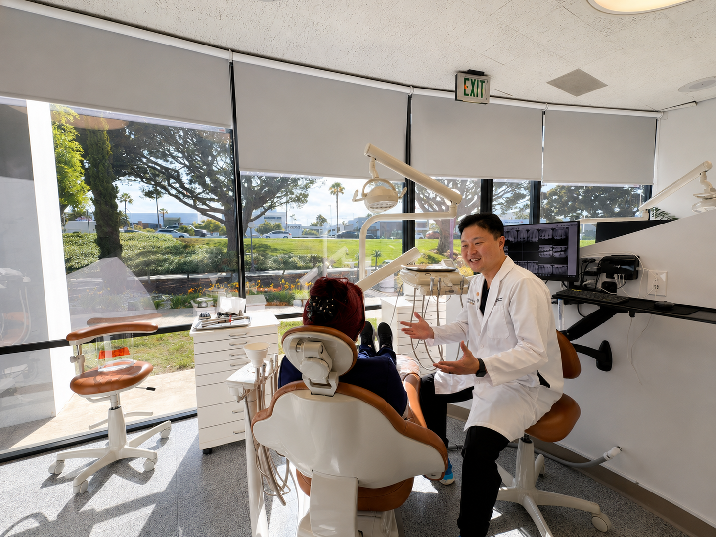 Dr. Choi consulting with a patient in the treatment room at Del Amo Dental Group, Torrance — floor-to-ceiling windows with garden views